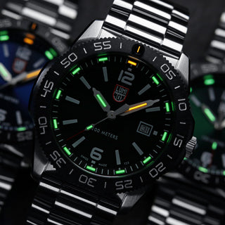 Close-up of a silver watch with a black face and green accents on a blurred background.